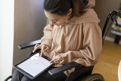 High angle view of woman with paraplegia using tablet pc while sitting on wheelchair at home