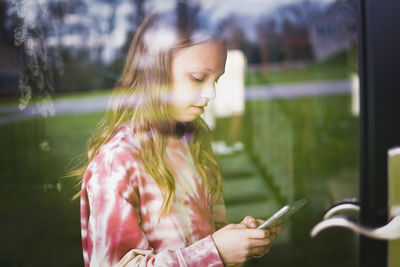 Girl using smart phone seen through window