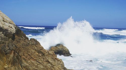 Waves breaking against sea against clear sky