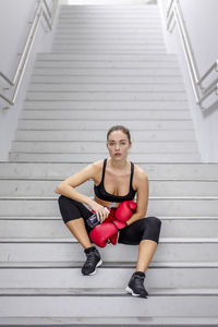 Confident young female athlete sitting on staircase at basement