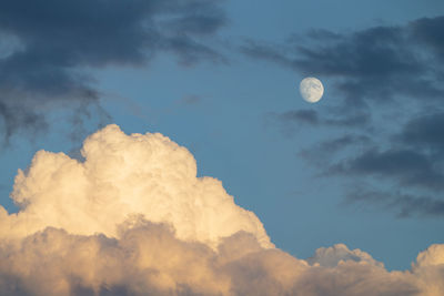 The photo shows a dramatically cloud formation with the moon in the sunset