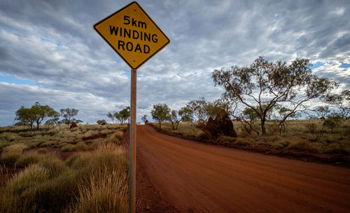 Road sign by trees against sky