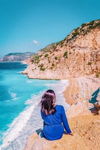 Rear view of woman sitting on cliff against beach