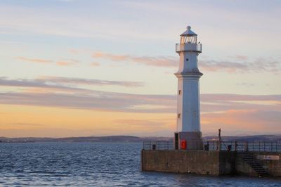 Lighthouse by sea against sky during sunset