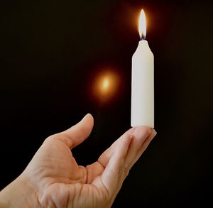 Close-up of hand holding lit candle against black background