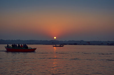 Silhouette boats in sea against orange sky