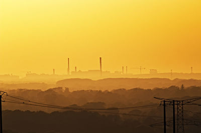 Silhouette of electricity pylons against orange sky