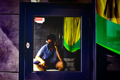Young man using mobile phone while sitting by window