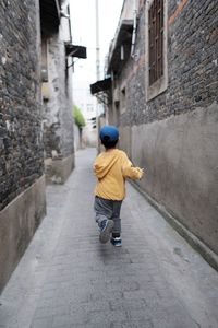 Rear view of boy walking on footpath amidst buildings
