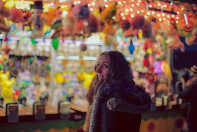 Side view of young woman looking away while standing in market at night