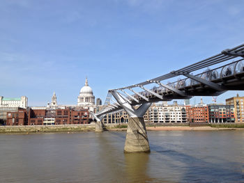 Millennium bridge over thames river by st paul cathedral against sky
