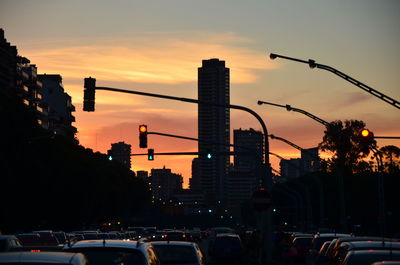 Cars parked in traffic amidst silhouette buildings against sky during sunset