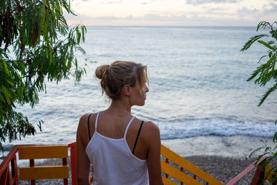 Side view of young woman sitting at beach against sky