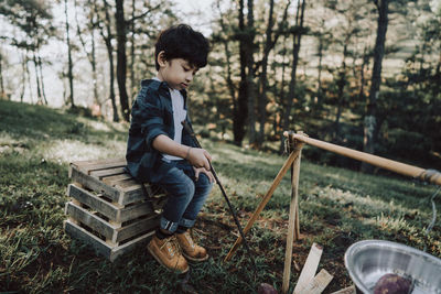 Boy preparing food while sitting on wood