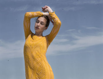 Young woman looking away while standing against sky