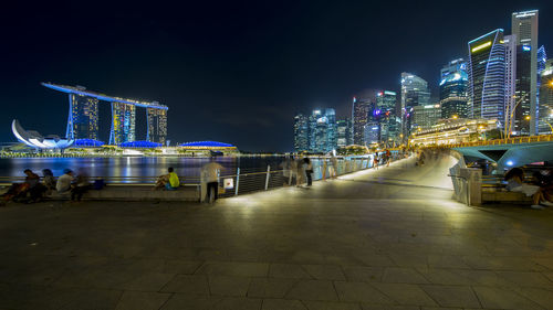 Illuminated city by river against sky at night