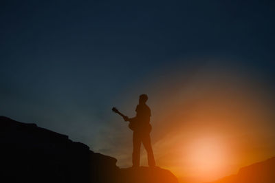 Silhouette people standing on rock against sky during sunset