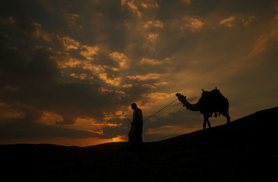 Silhouette woman walking on field against orange sky