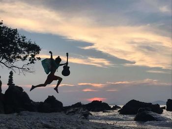 Man jumping on rock against sky during sunset