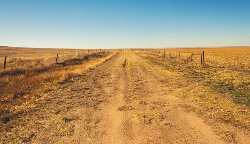 Dirt road amidst field against clear sky