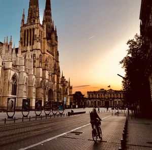 People walking on street amidst buildings against sky during sunset