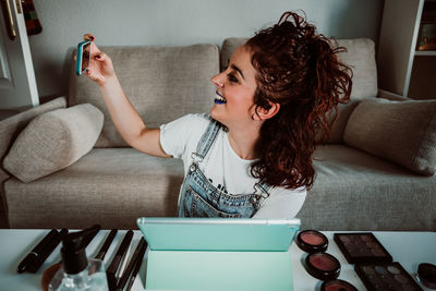 Smiling woman taking selfie while sitting with beauty products