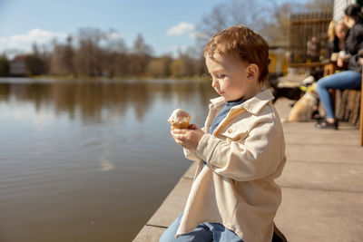 Little adorable boy sitting outdoors and eating ice cream. lake, water and sunny weather. 