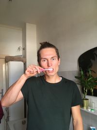 Portrait of man brushing teeth while standing at home