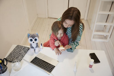 High angle view of blogger holding beauty product while sitting with daughter at table