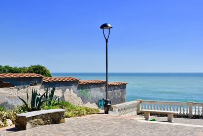 Street light by sea against clear blue sky