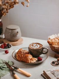 A cup of coffee with croissant and raspberry