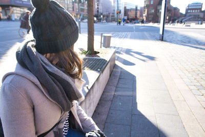 Rear view of woman sitting on footpath in city