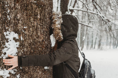 Woman in jacket embracing the wood in nature, winter time with snow