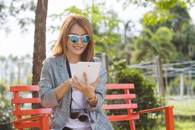 An asian woman is very happy to watch a tablet on a bench.