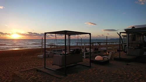 Chairs on beach against sky during sunset