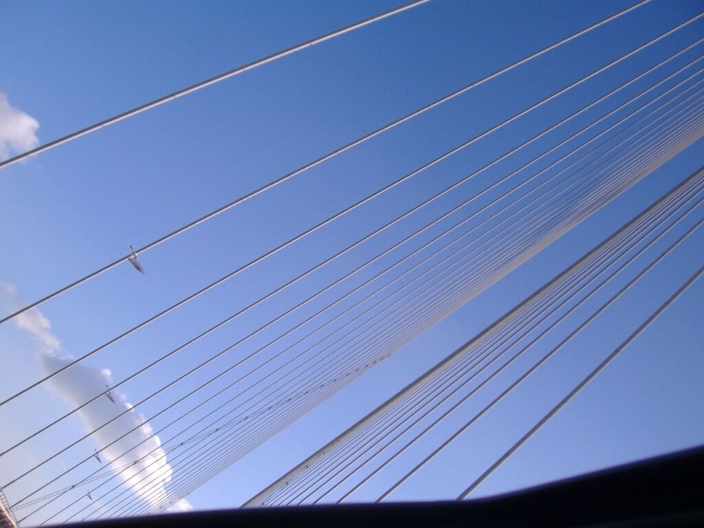 low angle view, connection, blue, built structure, sky, cable, architecture, power line, clear sky, electricity, no people, modern, day, outdoors, part of, bridge - man made structure, glass - material, power supply, electricity pylon, building exterior