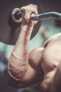 Close-up of shirtless muscular man lifting barbell in gym