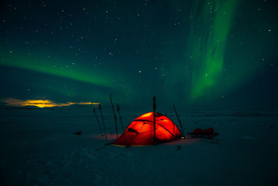 Tent on snow covered land against sky at night