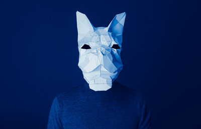 Person wearing french bulldog origami paper mask against blue background