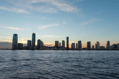 Sea by modern buildings in city against sky