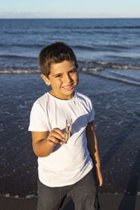 Portrait of boy holding crab standing in sea