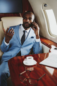 Elegant businessman talking on smart phone while traveling in airplane