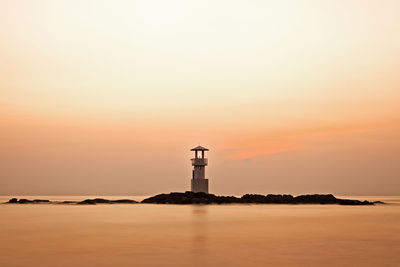 Lighthouse by sea against sky during sunset