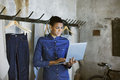 Smiling female fashion designer using laptop while standing at workshop