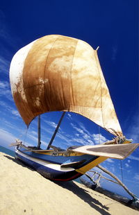 Low angle view of boat moored at beach against blue sky on sunny day