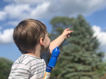 Rear view of boy with arms raised against sky