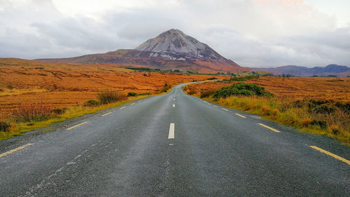 Road leading towards mountains against sky