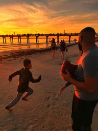 People playing on beach against sky during sunset