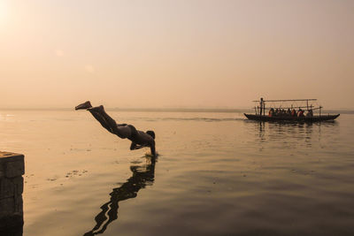 Full length of shirtless man diving in river during sunset