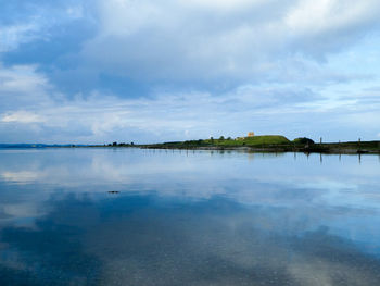 Calm reflective sea with castle ruin in the distance